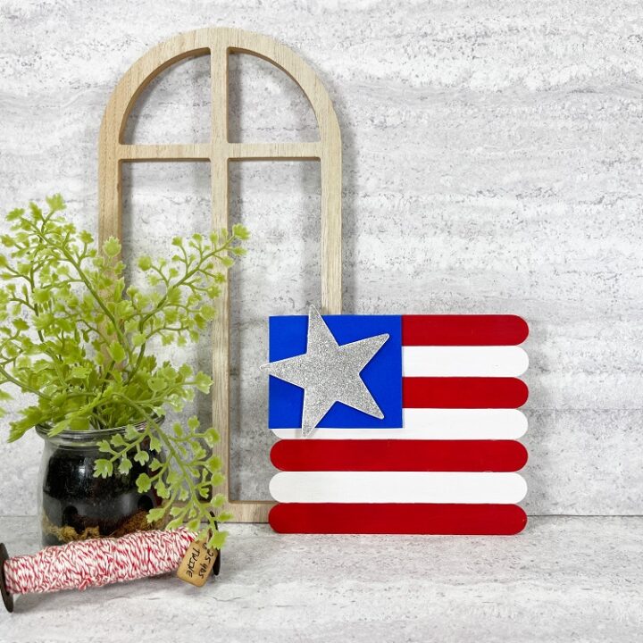 Red and white painted jumbo craft sticks made to look like an American flag with a blue square and silver sparkly star glued onto it.