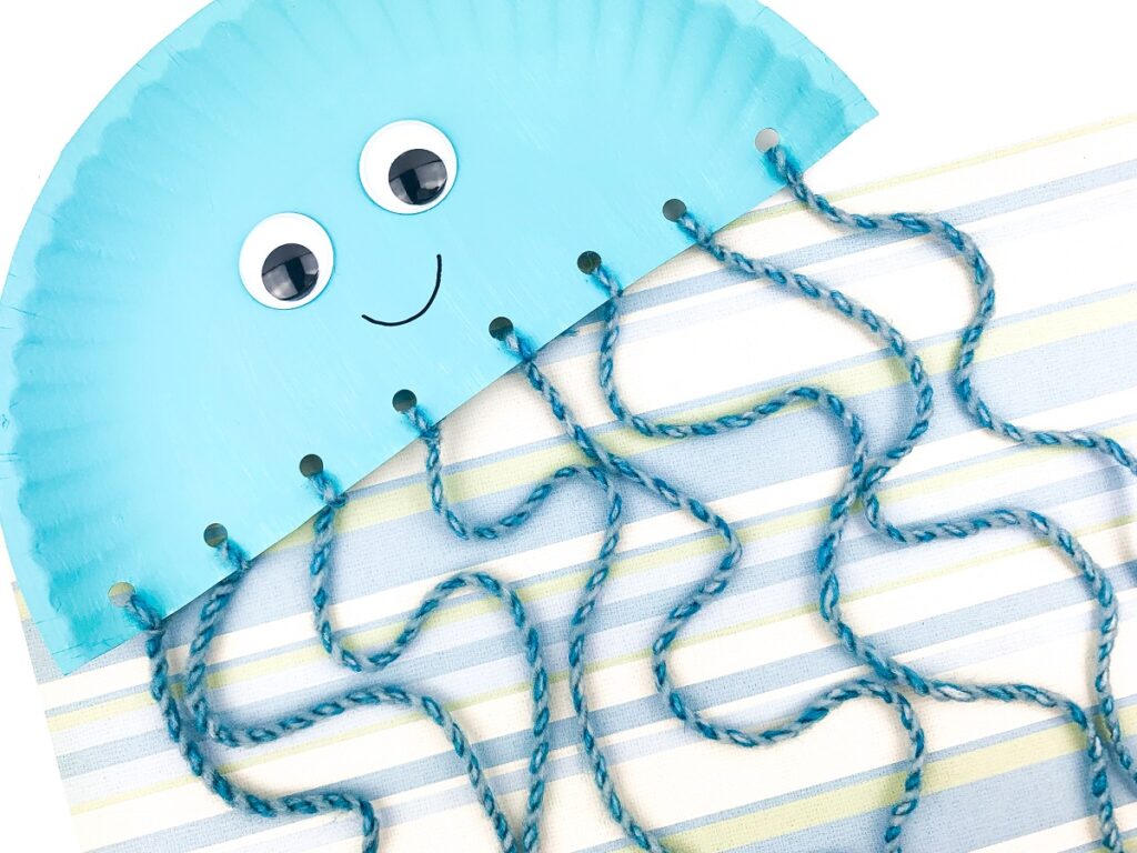 Close view of finished jellyfish craft made with paper plate and yarn.