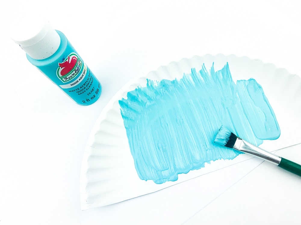Bottle of Aqua Sky blue paint to the left of half of a paper plate being painted blue.