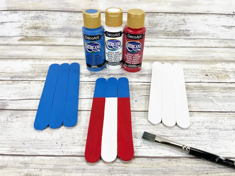 Three sets of jumbo popsicle sticks. One painted all blue, one painted red and white vertical stripes with top section all blue. Another one is completely white.