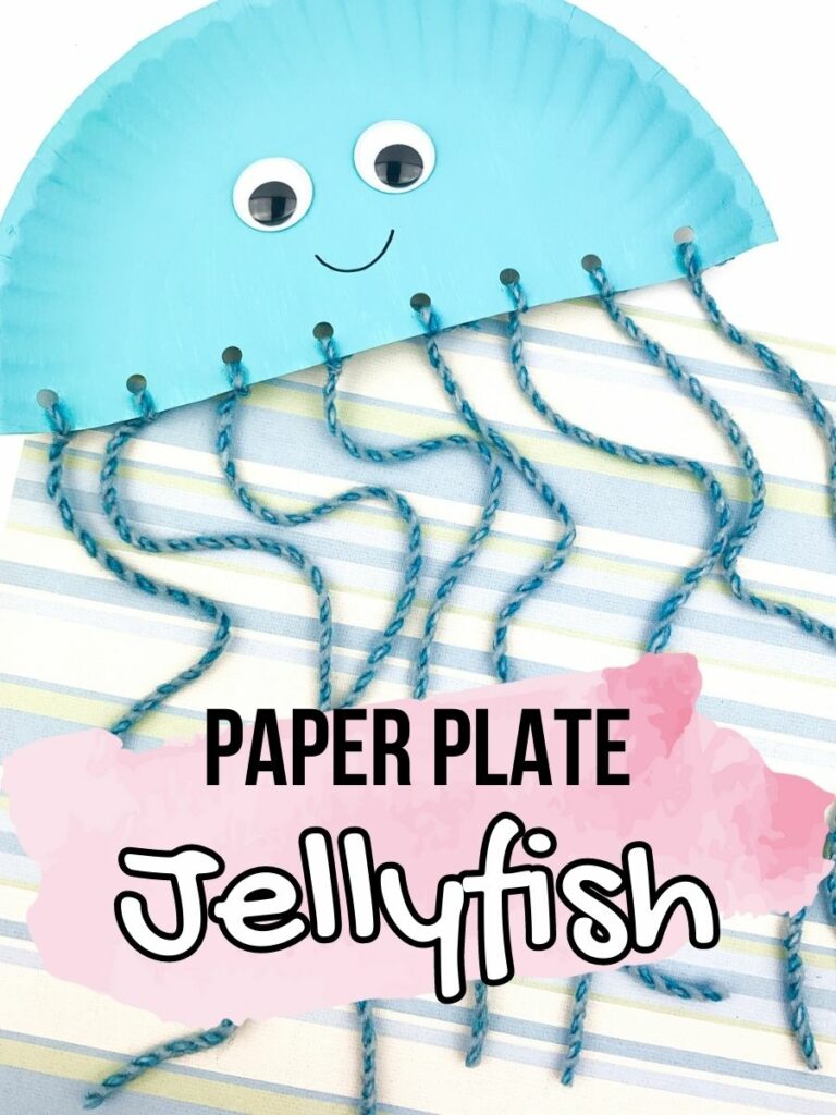 Half of a paper plate painted light blue with googly eyes and a drawn on smile and yarn tied to holes along the flat bottom of plate to look like a jellyfish. Blue yarn tentacles laying over striped scrapbook paper. Text near bottom of photo says Paper Plate Jellyfish.