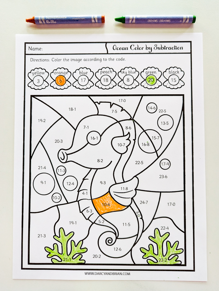 Top down view of seahorse color by subtraction worksheet partially colored in with crayons. Two crayons lay along the top edge of the paper.