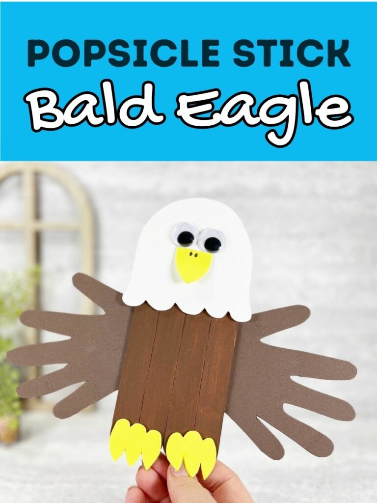Black and white text on light blue background at top of image says Popsicle Stick Bald Eagle. Underneath is a close view of a hand holding up a finished craft project made with popsicle sticks and craft foam pieces.