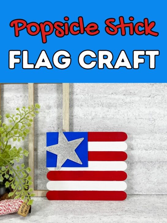 Red and white text on light blue background says Popsicle Stick Flag Craft above a small flag made out of painted craft sticks, blue craft foam, and a glittery wooden star.