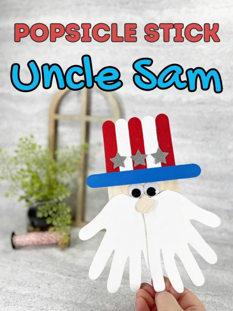 Red and blue text outlined in black at top of photo says Popsicle Stick Uncle Sam. Hand holding up Uncle Sam head made out of popsicle craft sticks and handprint beard.