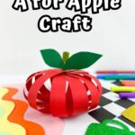White text with thick black outline says A for Apple Craft above apple made out of paper strips sitting on top of assorted supplies and colored paper.