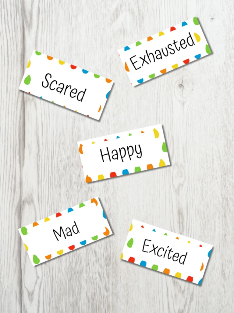 Mockup of five word cards spread out on a white wood table. The cards say scared, exhausted, happy, mad, and excited.