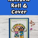 White text on dark blue background at the top says Rainbow Roll & Cover. Underneath is a photo of the game printed out on a piece of paper, laying on top of a blue folder. There is a six sided die and mini rainbow erasers too.