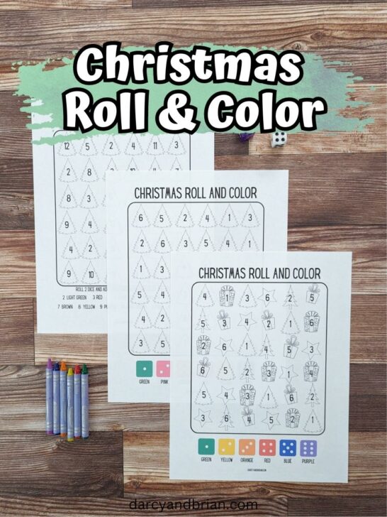 Three different roll and color Christmas printable pages laid out in a diagonal line, overlapping each other. There are crayons and dice nearby. At the top of the photo is white text over a green splash of color. Text says Christmas Roll & Color.