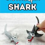 Bright blue box at top with white text outlined in black says Clothespin Shark. Two finished sharks made from painting clothespins and gluing on felt fins, tails, googly eyes and paper teeth. One is painted light gray and one is dark gray and being pinched to open its mouth.