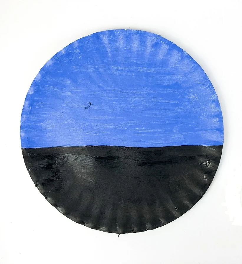 Round paper plate painted half blue and half black for the sky and road.