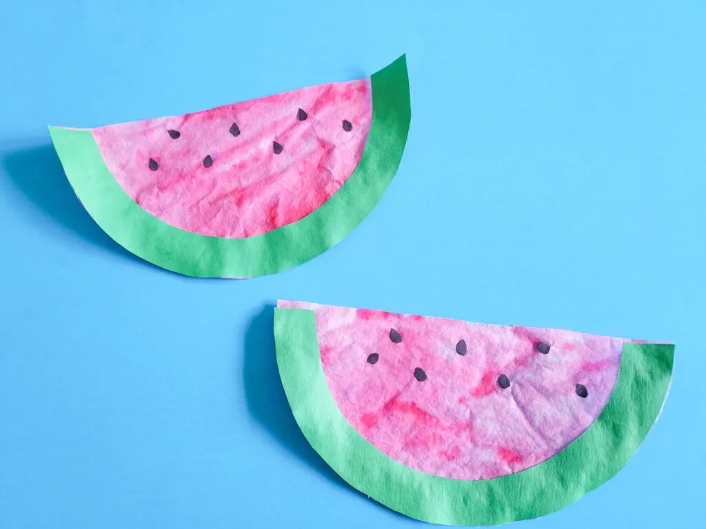 Two coffee filter watermelons finished and laying on a bright blue background.