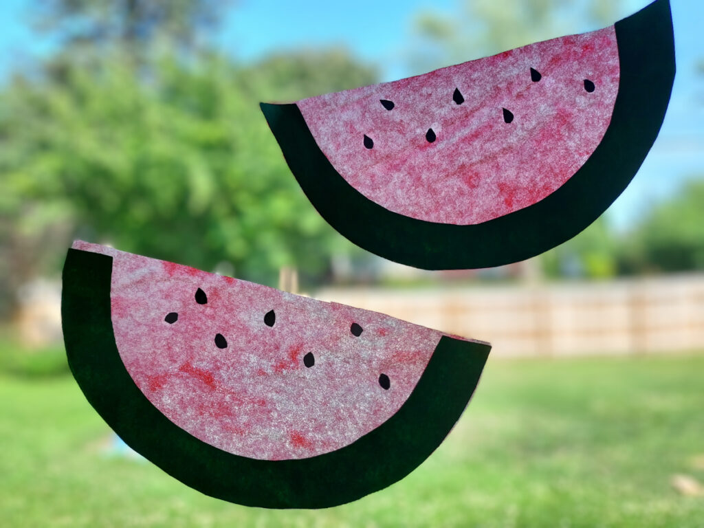 Two coffee filter watermelons hanging in a sunny window as suncatchers.