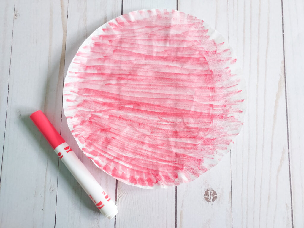 Round coffee filter laying flat and colored with a red marker. Marker laying next to it.