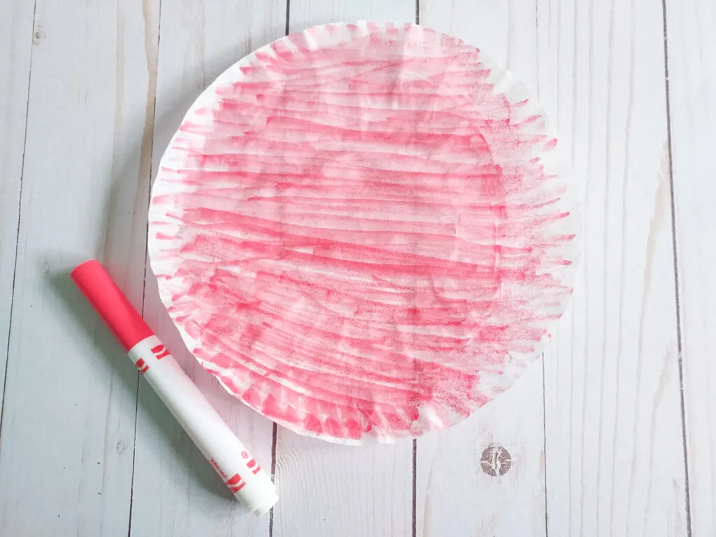 Round coffee filter laying flat and colored with a red marker. Marker laying next to it.