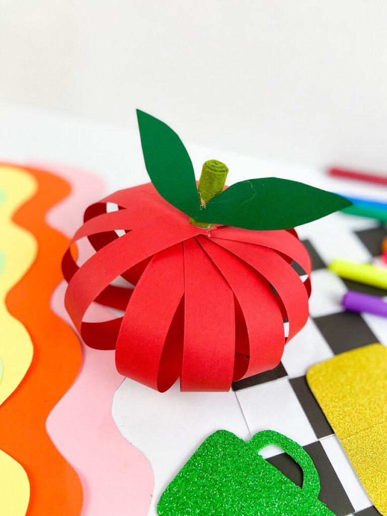 Angled overhead view of a craft project to make an apple out of strips of construction paper.