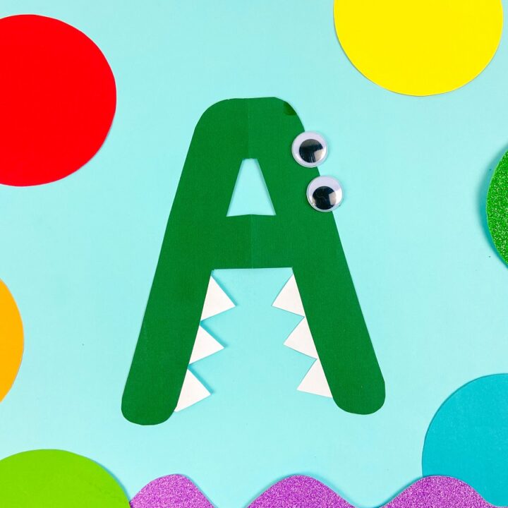 Completely finished alphabet alligator craft. Bright colored shapes are arranged around it for decoration.