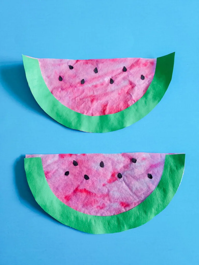 Overhead view of two completed coffee filter watermelon crafts lined up vertically.