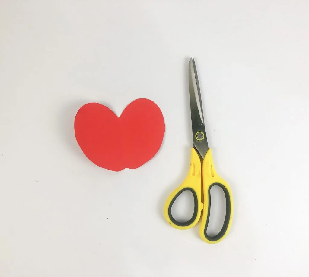Red paper cut into an apple shape laying next to a pair of scissors.