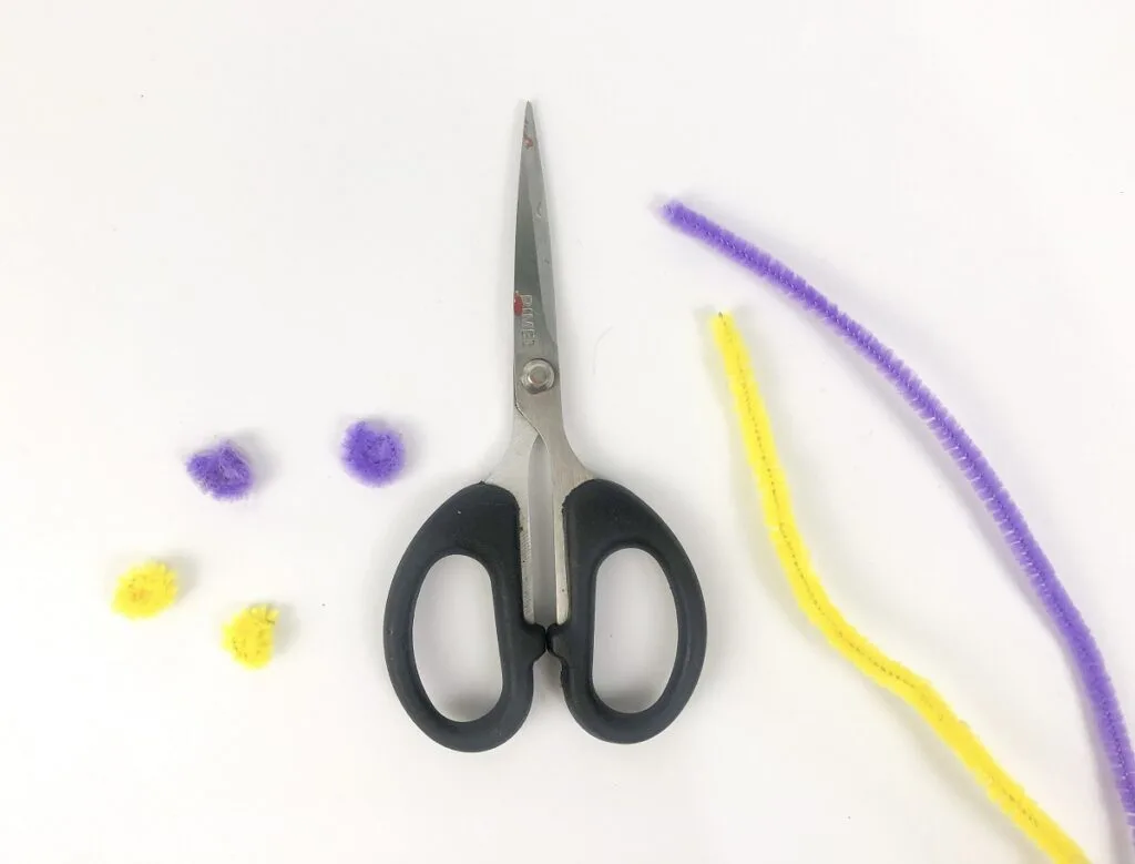 Pieces of purple and yellow chenille stems cut off and rolled up. Pair of scissors lays in the middle of the stems.