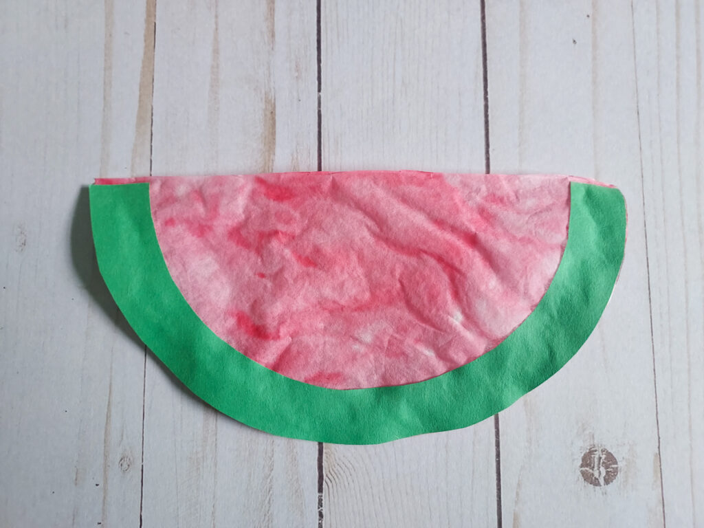 Green paper glued along outer edge of reddish pink colored coffee filter.