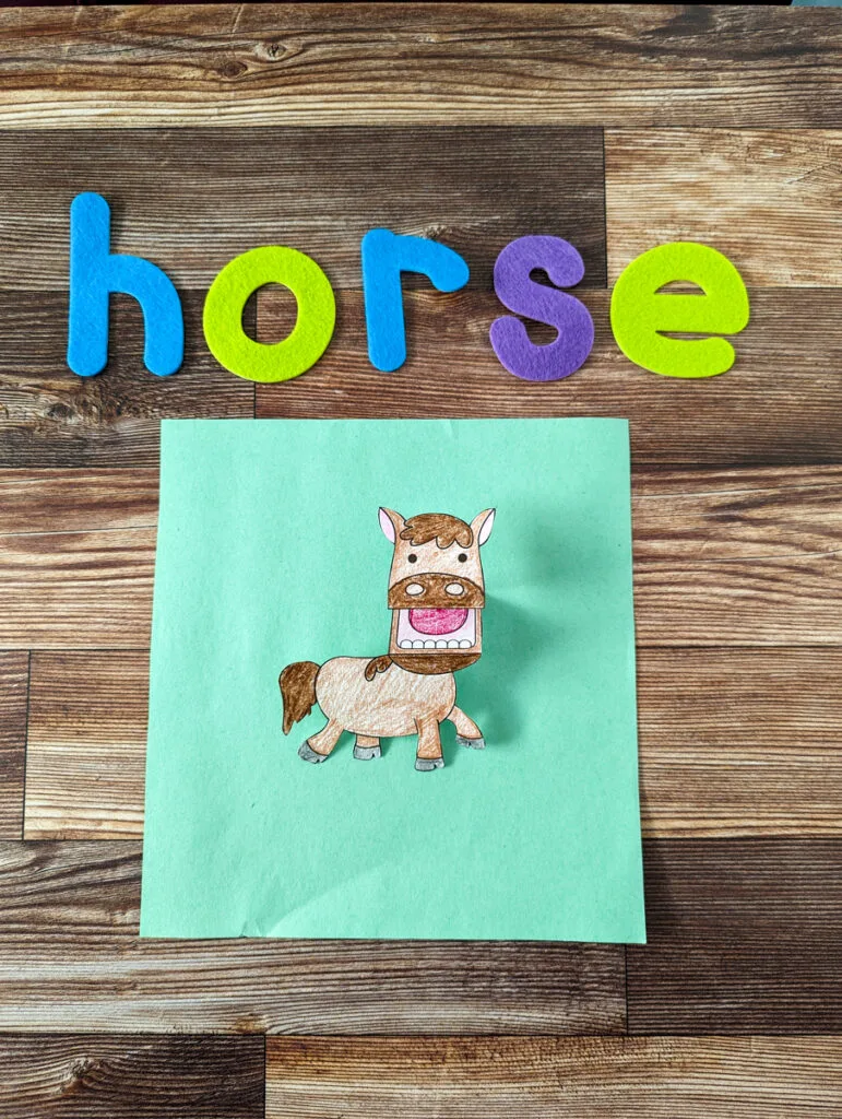 Felt letters in assorted colors spell the word horse above a completed horse finger puppet laying on a piece of light green paper.