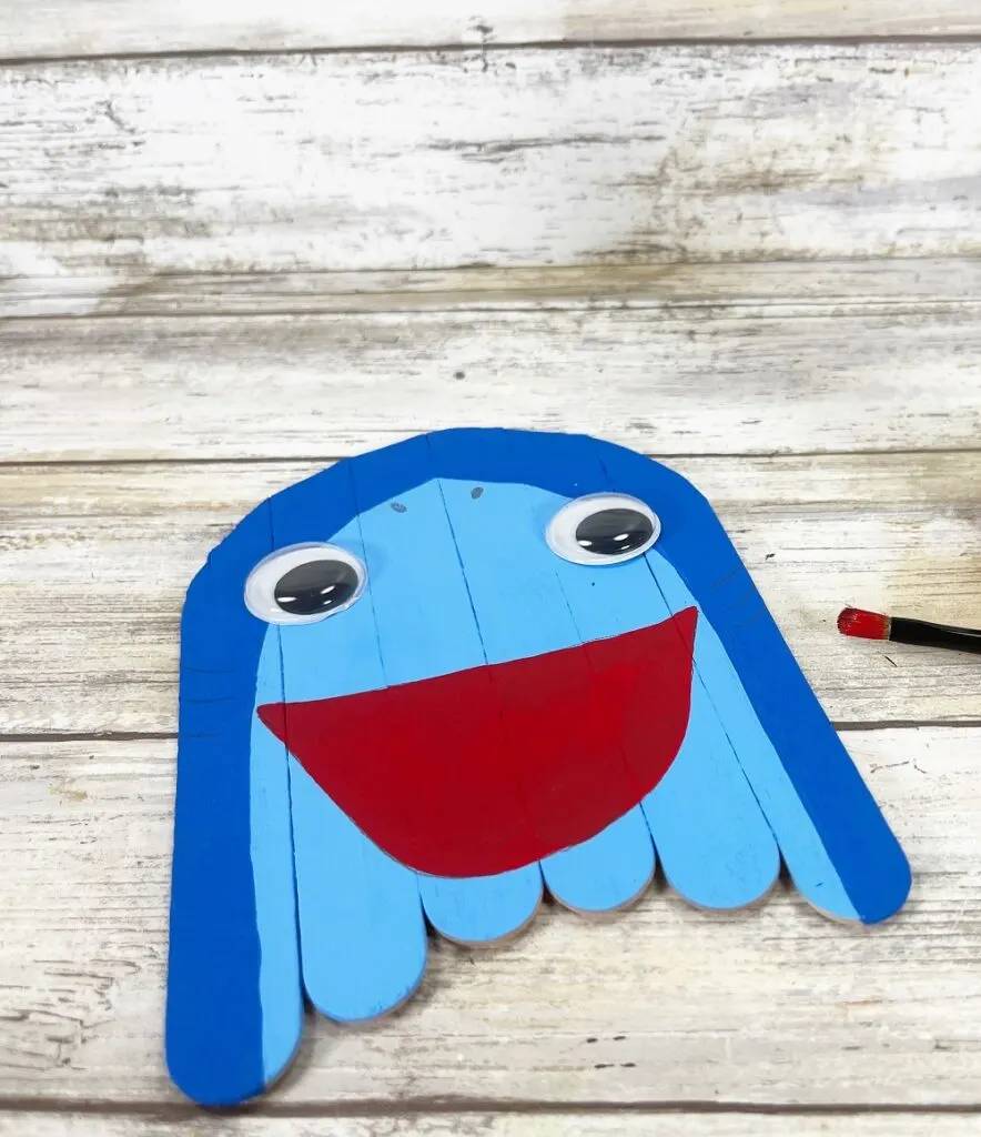 Jumbo craft sticks painted two tones of blue to look like a shark head. Two googly eyes glued on and large open mouth painted red.