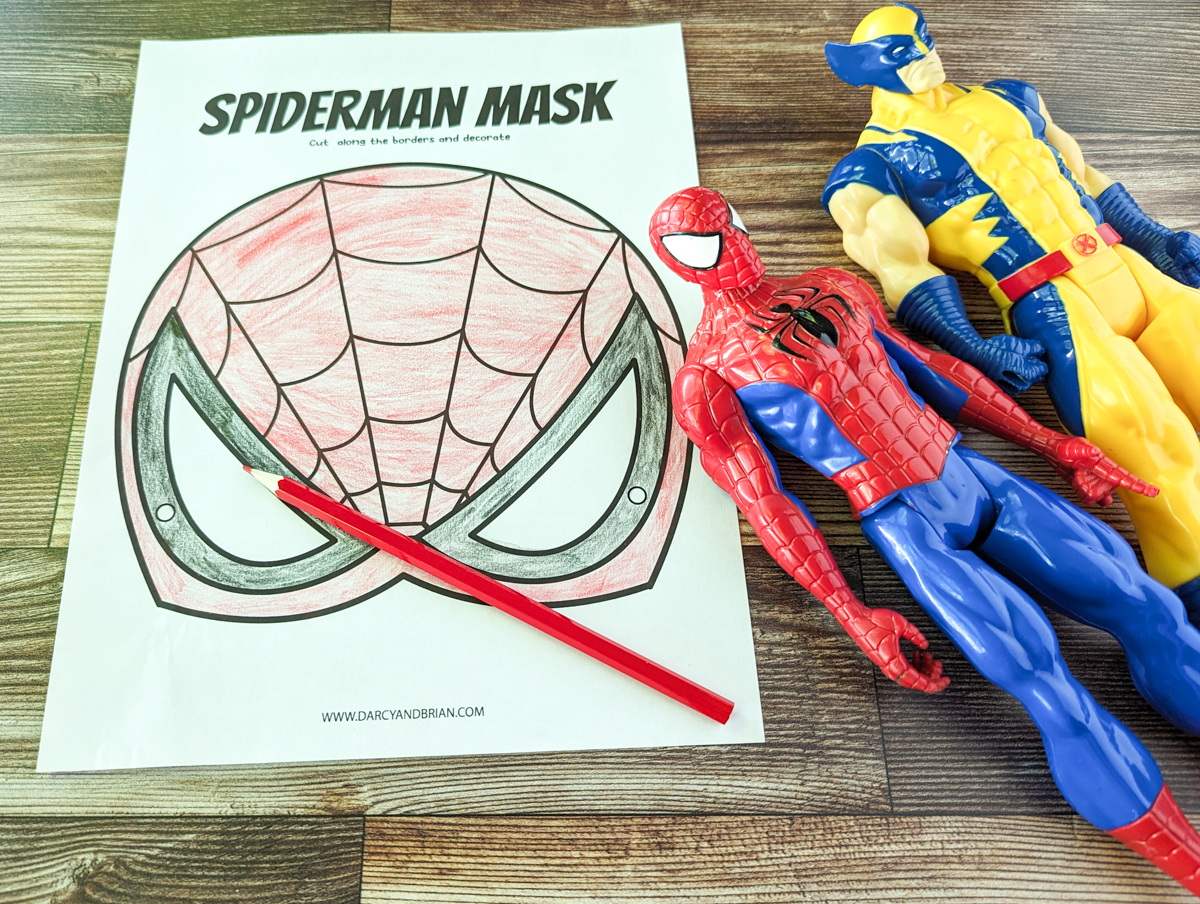 Printed out Spider Man mask colored in with red and black colored pencils. Spider Man and Wolverine action figures lay next to the page.