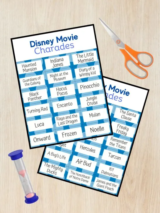Mockup showing two of the pages from the Disney Movie Charades printable game overlapping on a desk. A pair of scissors and a sand timer are next to the page preview.