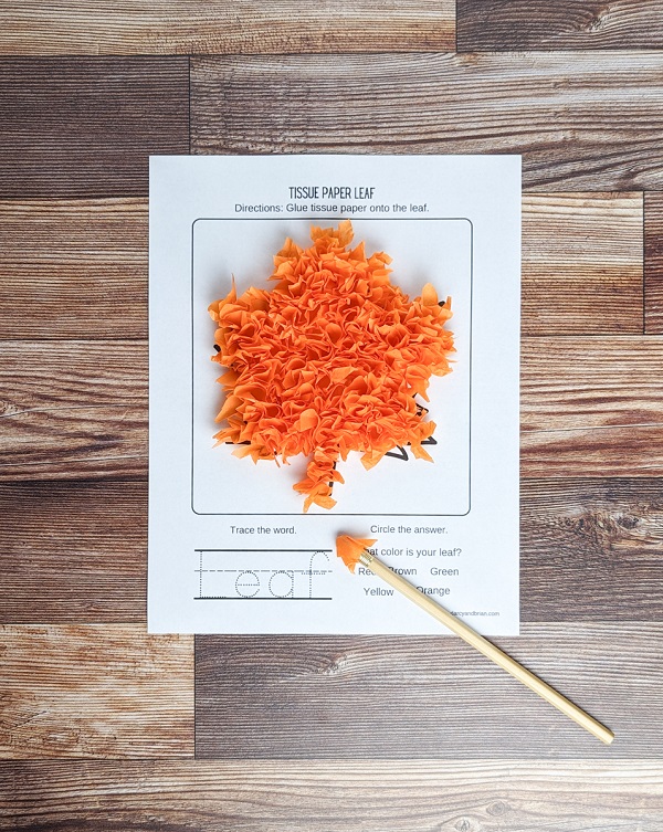 Orange tissue paper pieces glued down in a way that the paper is sticking up and giving it a fluffy textured look. A pencil with a piece wrapped around the eraser end is laying on the paper.