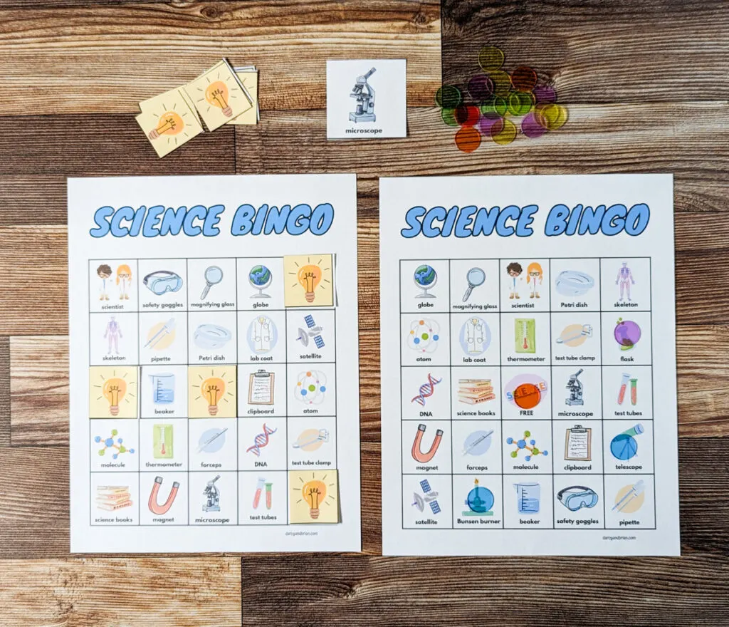 Two science themed bingo cards printed out and laying side by side. One has spaces covered with the printable lightbulb markers and the other with colorful plastic bingo chips.