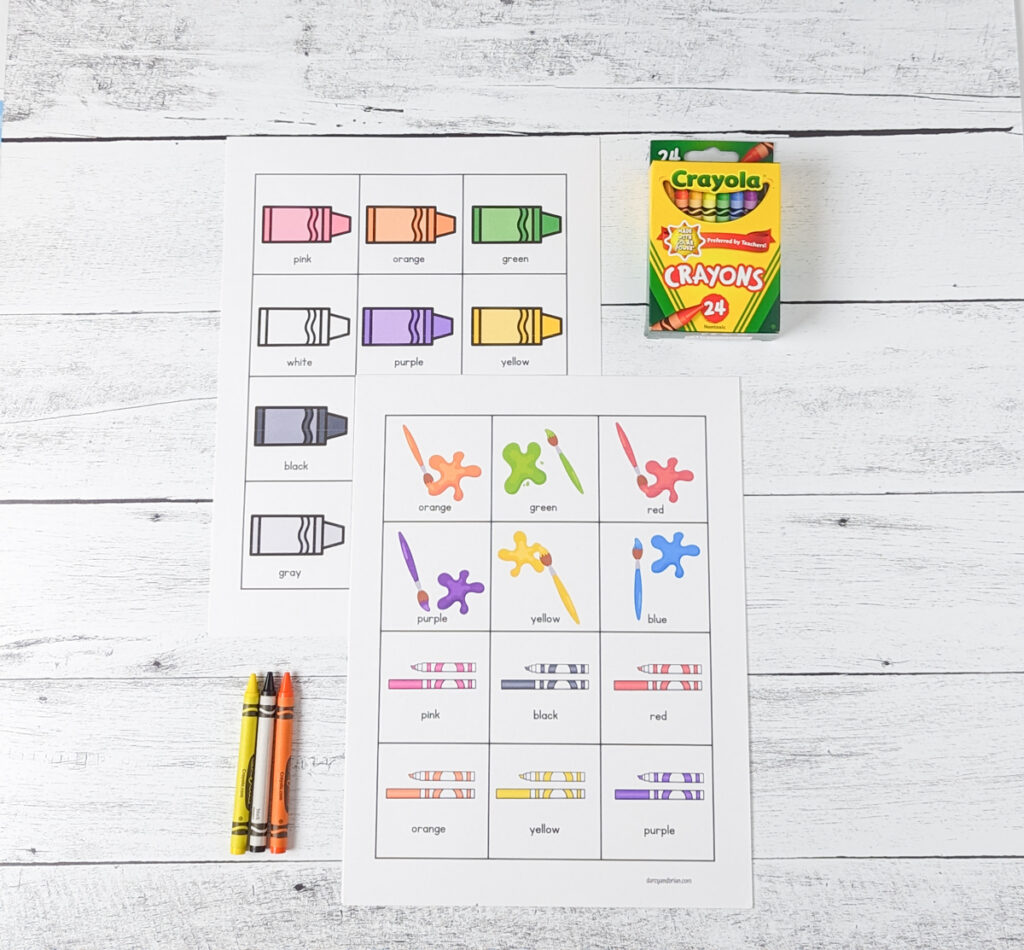 Two pages of color matching game printed out and overlapping. A box of crayons and a few crayons lay nearby.