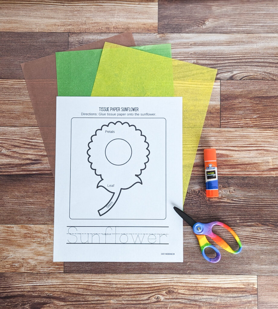 Sunflower craft template printed out and laying over brown, green, and yellow tissue paper. A glue stick and scissors are next to the paper.