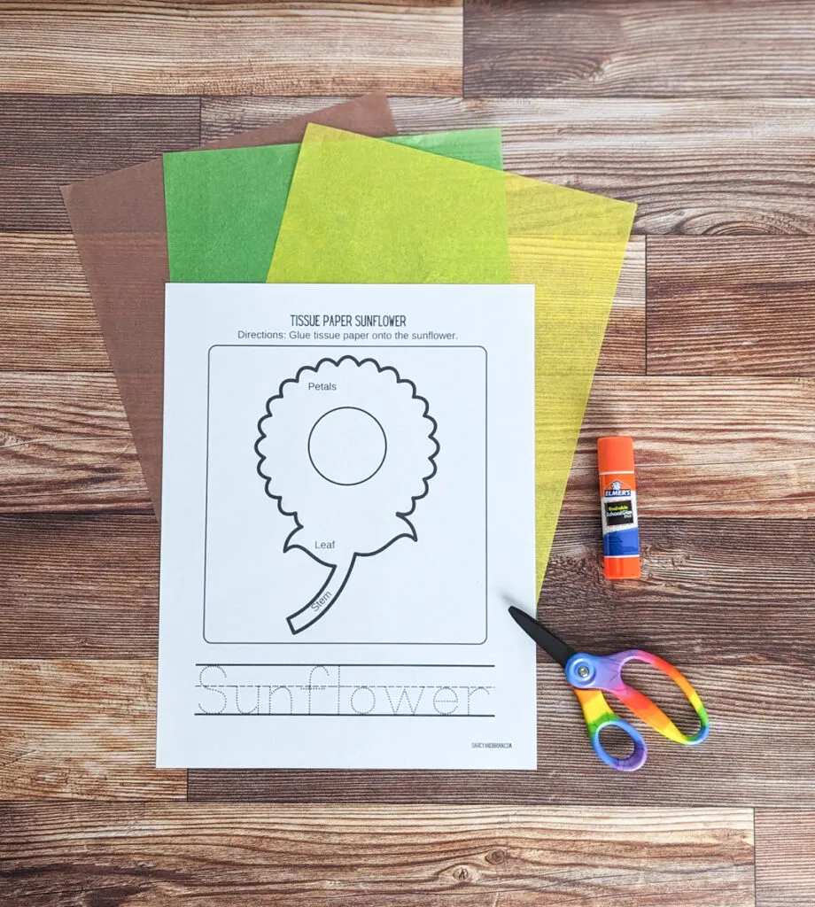 Sunflower craft template printed out and laying over brown, green, and yellow tissue paper. A glue stick and scissors are next to the paper.