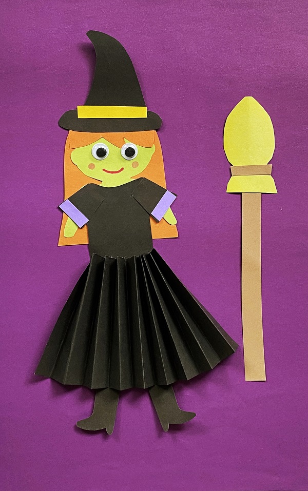 Witch with orange hair and green skin made out of construction paper with a black accordion fold skirt.
