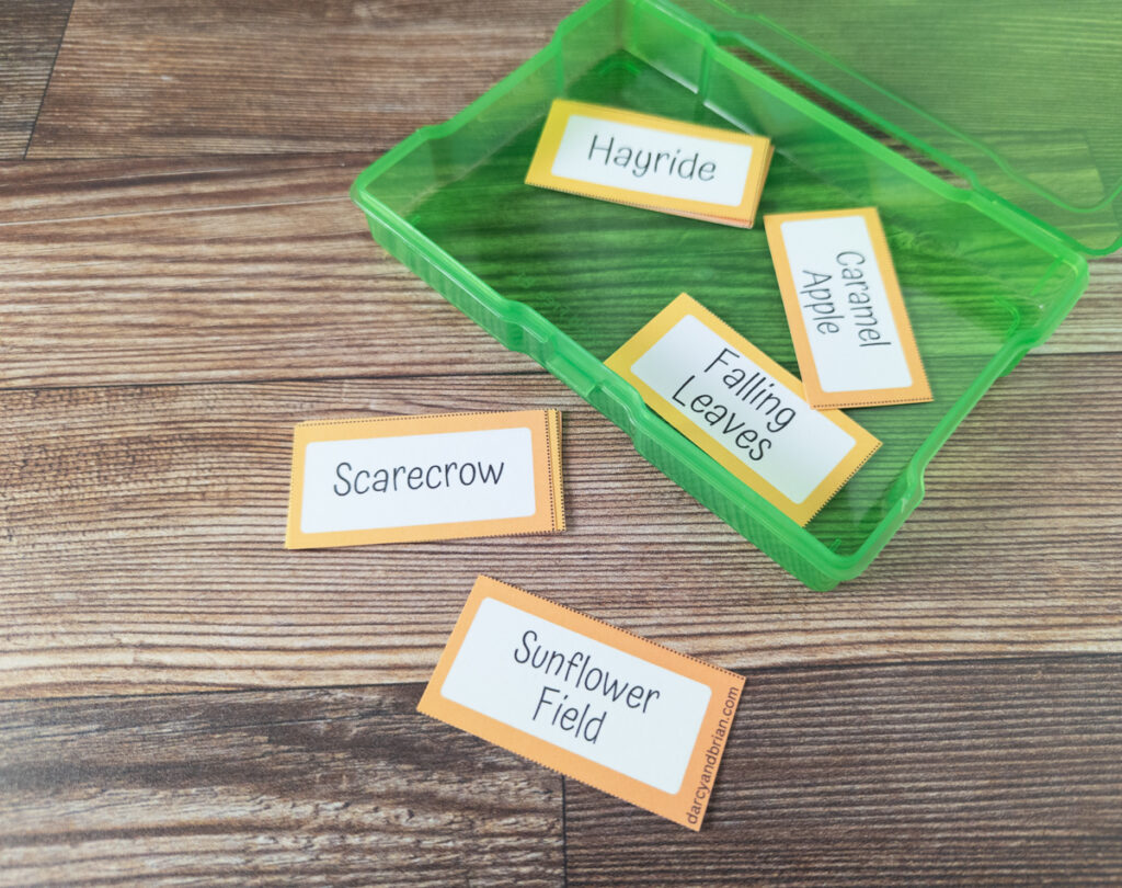 Assorted fall themed pictionary word cards cut out and laying on table and inside green task card box.
