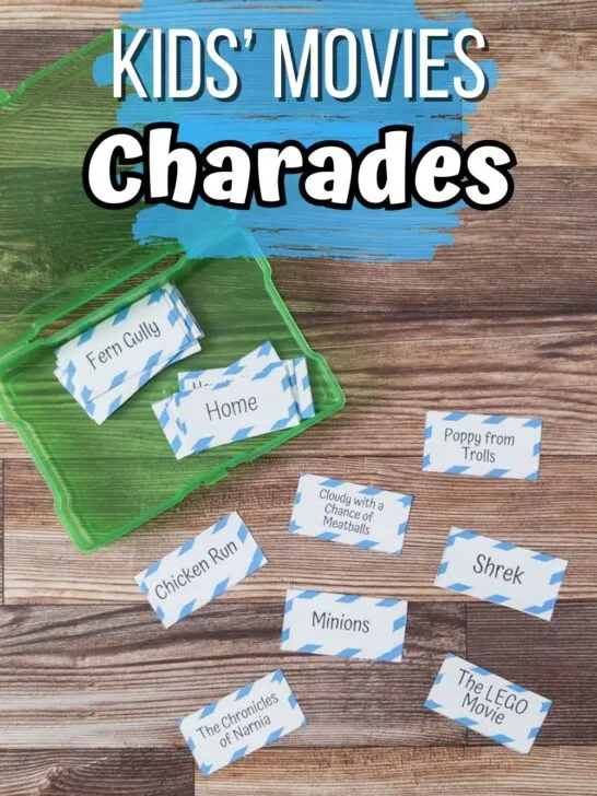 Overhead view of assorted charades cards with kid movie titles cut out and laying on table. Some cards are in an open green task box. Top of the photo has white text on a blue splash of color that says Kids' Movies Charades.