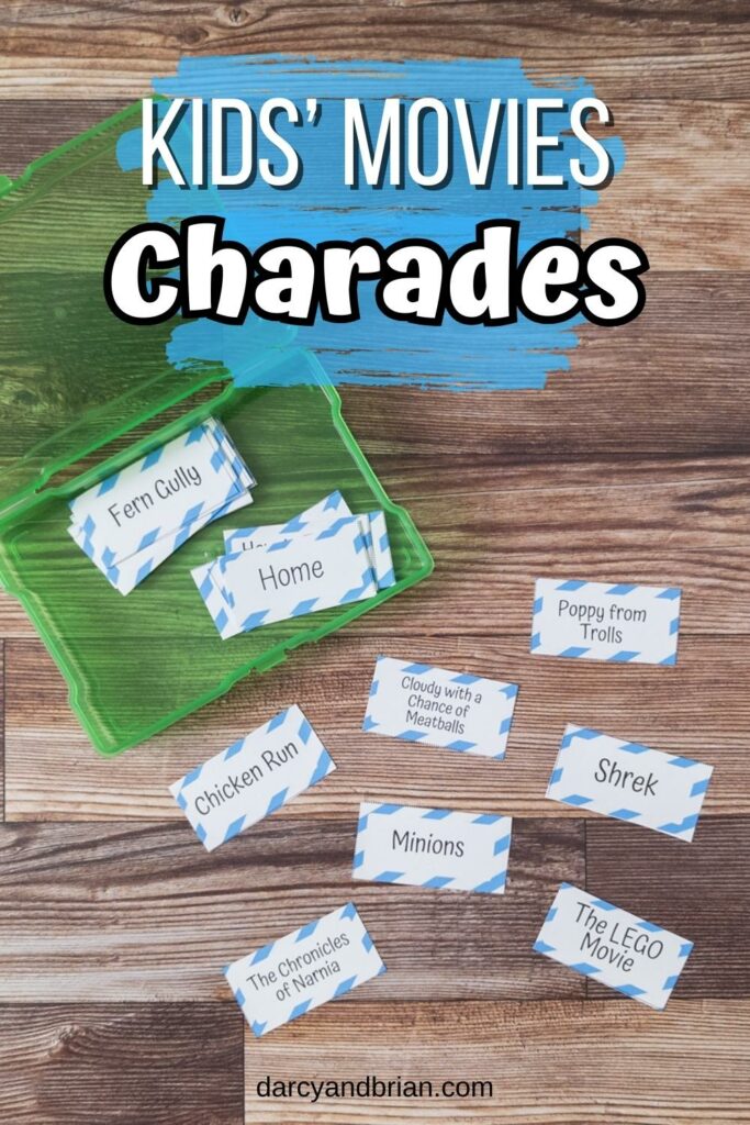 Overhead view of assorted charades cards with kid movie titles cut out and laying on table. Some cards are in an open green task box. Top of the photo has white text on a blue splash of color that says Kids' Movies Charades.