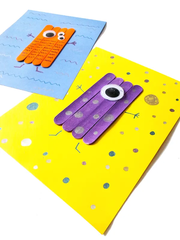 Close view at an angle of orange and purple monsters made with craft sticks on cardstock paper.
