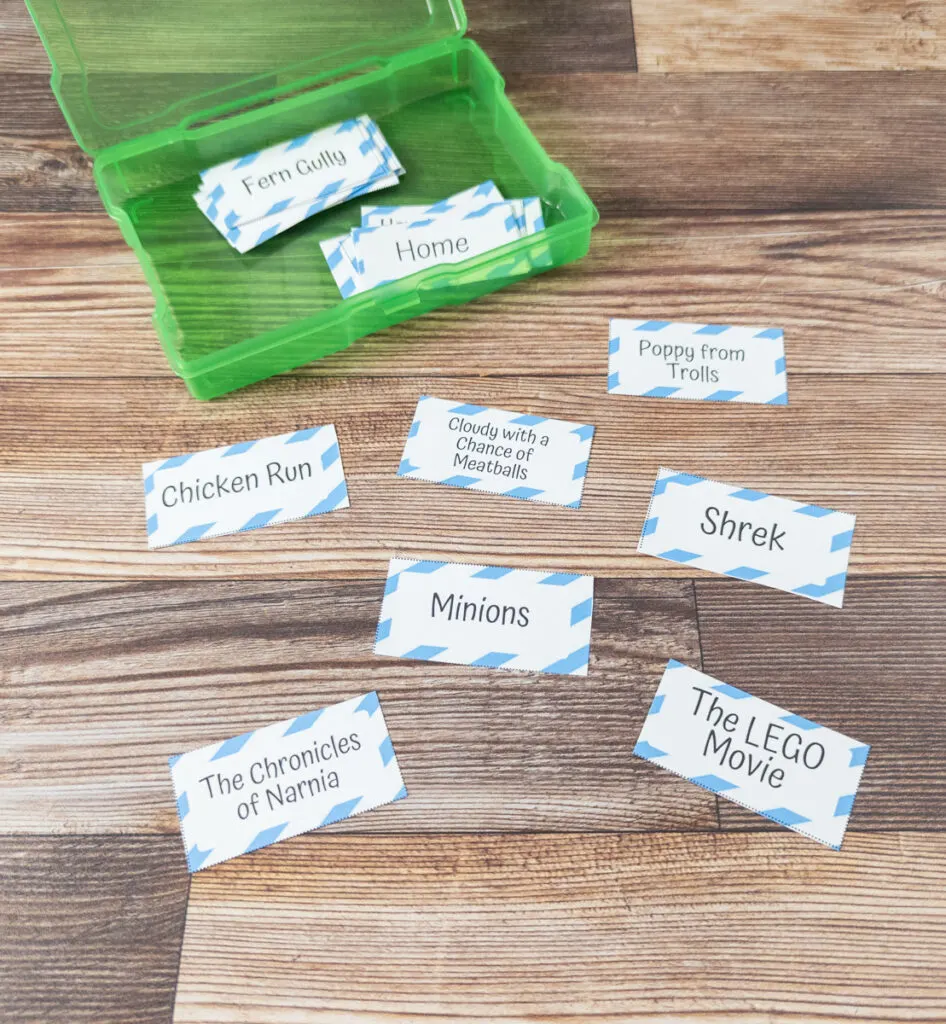 A few charades printable cards spread out on the table next to a green task box.