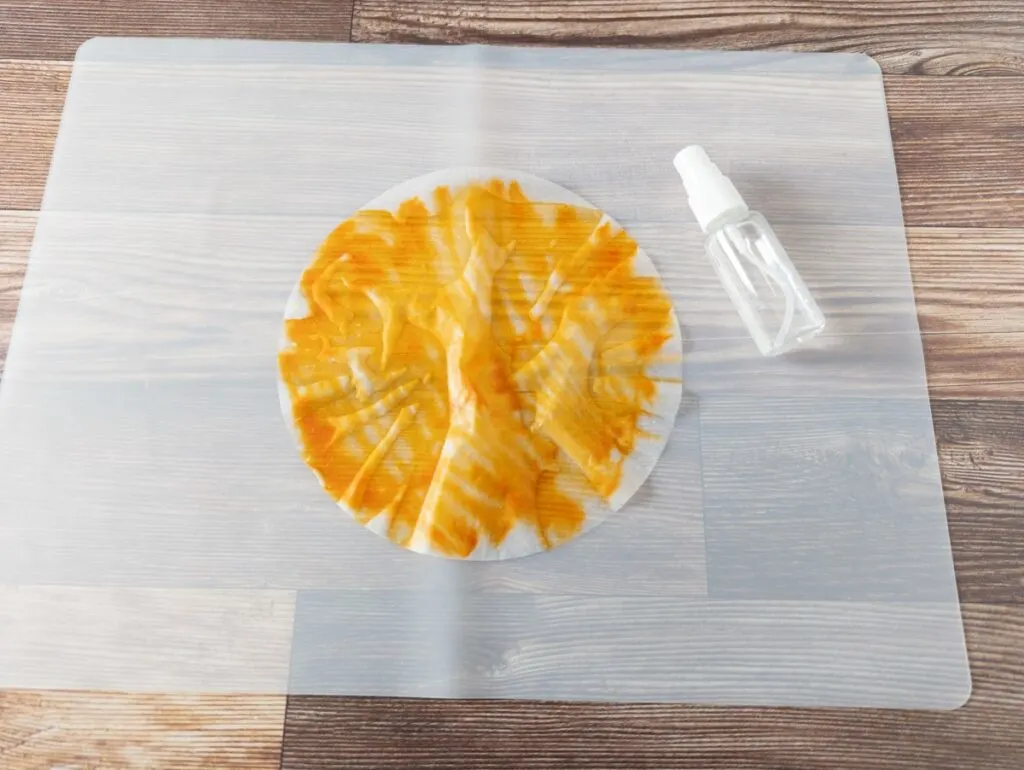 Orange colored coffee filter sprayed with water using a fingertip sprayer to blend the ink.