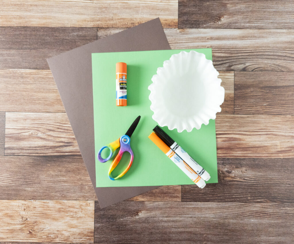 Craft supplies to make coffee filter pumpkins: Brown and green construction paper, orange and black markers, coffee filters, scissors, and glue stick.