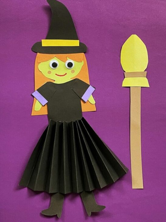 Witch with orange hair and green skin made out of construction paper with a black accordion fold skirt.