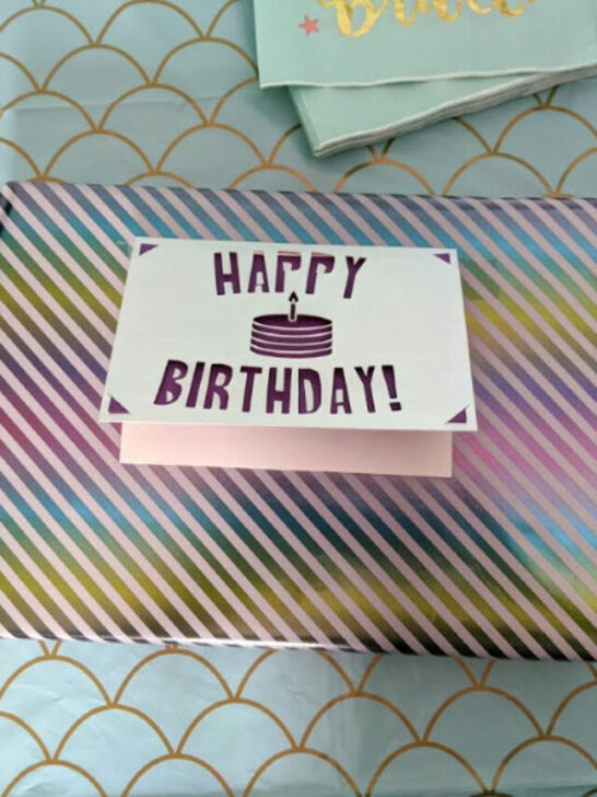 Silver and purple cutout birthday card attached to a wrapped present.