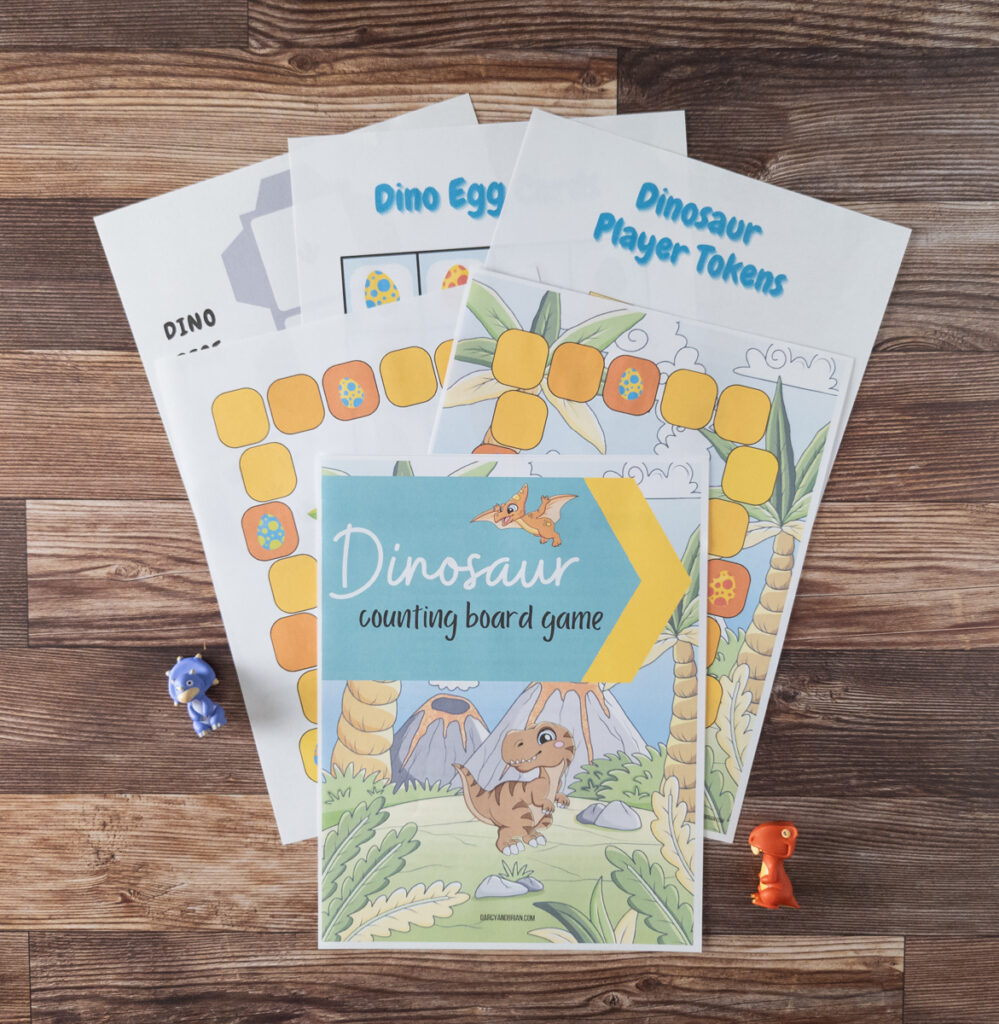 Top down view of dinosaur counting game pages printed and fanned out on table with two small dinosaur toys on either side.