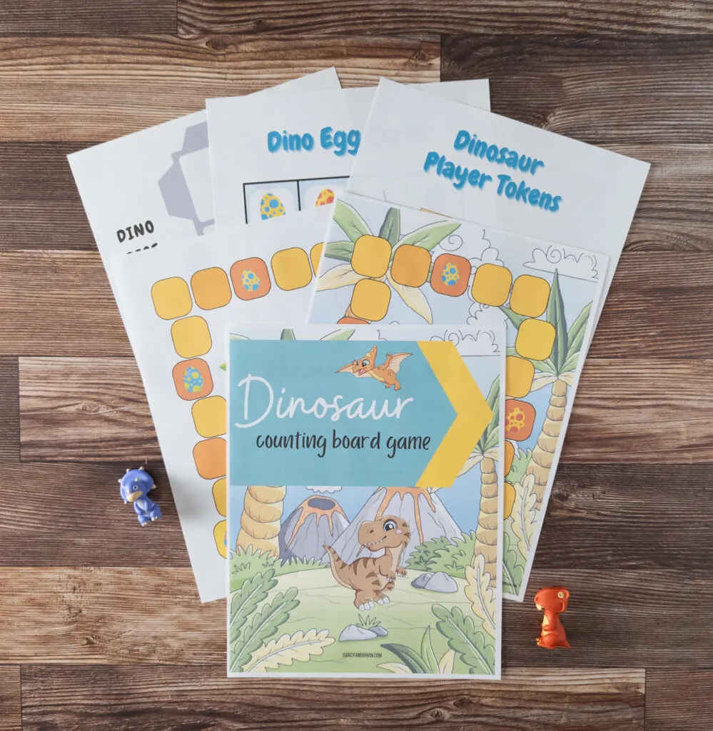 Top down view of dinosaur counting game pages printed and fanned out on table with two small dinosaur toys on either side.