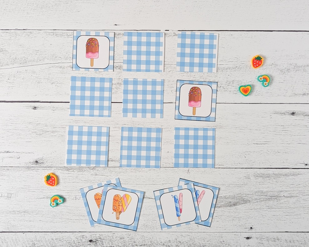A nine square array laid out with two matching popsicle cards face up. A few small cute erasers lay by the game.