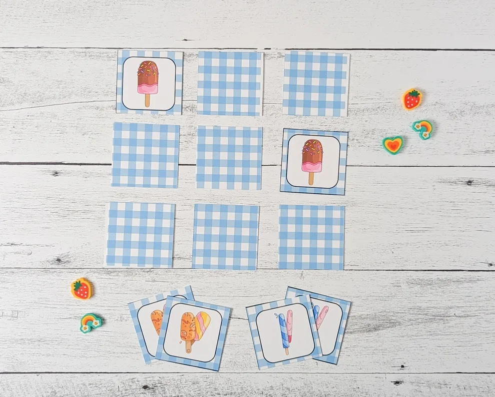 A nine square array laid out with two matching popsicle cards face up. A few small cute erasers lay by the game.