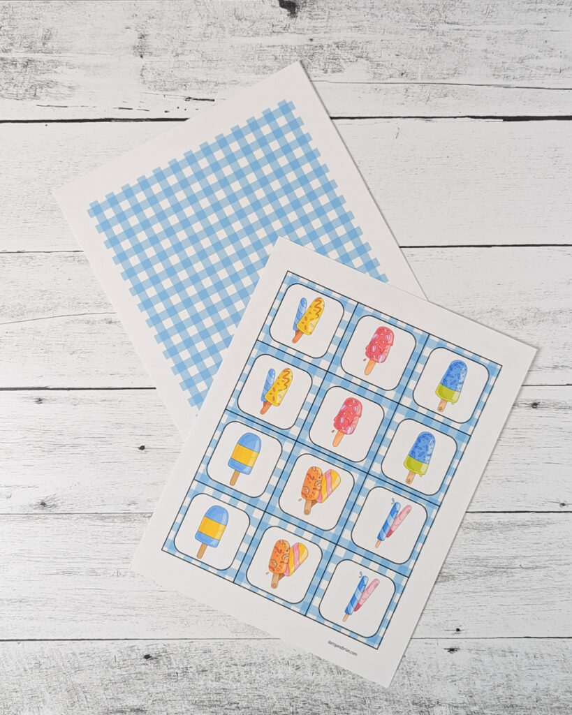 One page of popsicle game cards printed out and laying overlapping the back pattern page which is a blue plaid.
