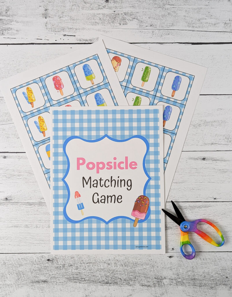 Cover page and two pages of popsicle matching game cards printed out and laying fanned out on table. Pair of rainbow handled scissors next to it.